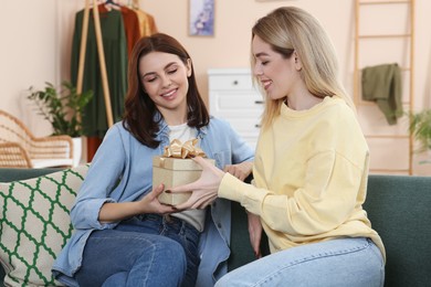 Smiling young woman presenting gift to her friend at home