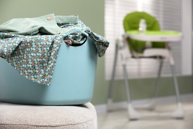 Laundry basket with baby clothes on light ottoman in child room, space for text