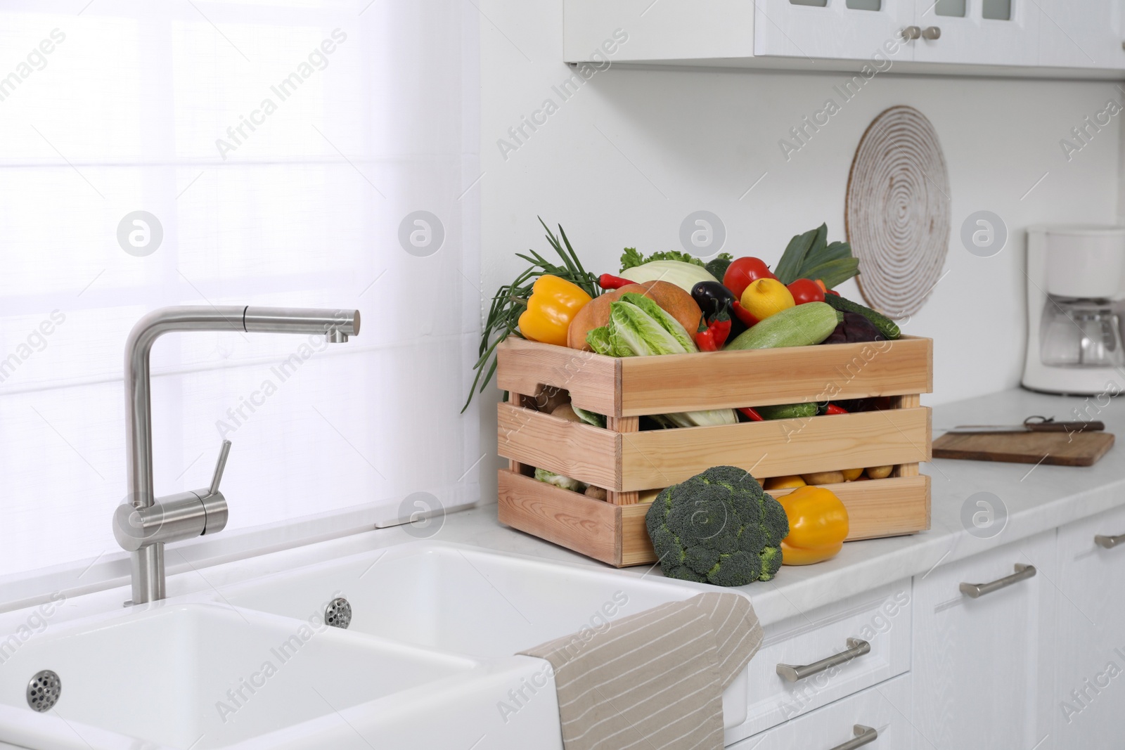 Photo of Wooden crate with fresh ripe vegetables near sink in kitchen