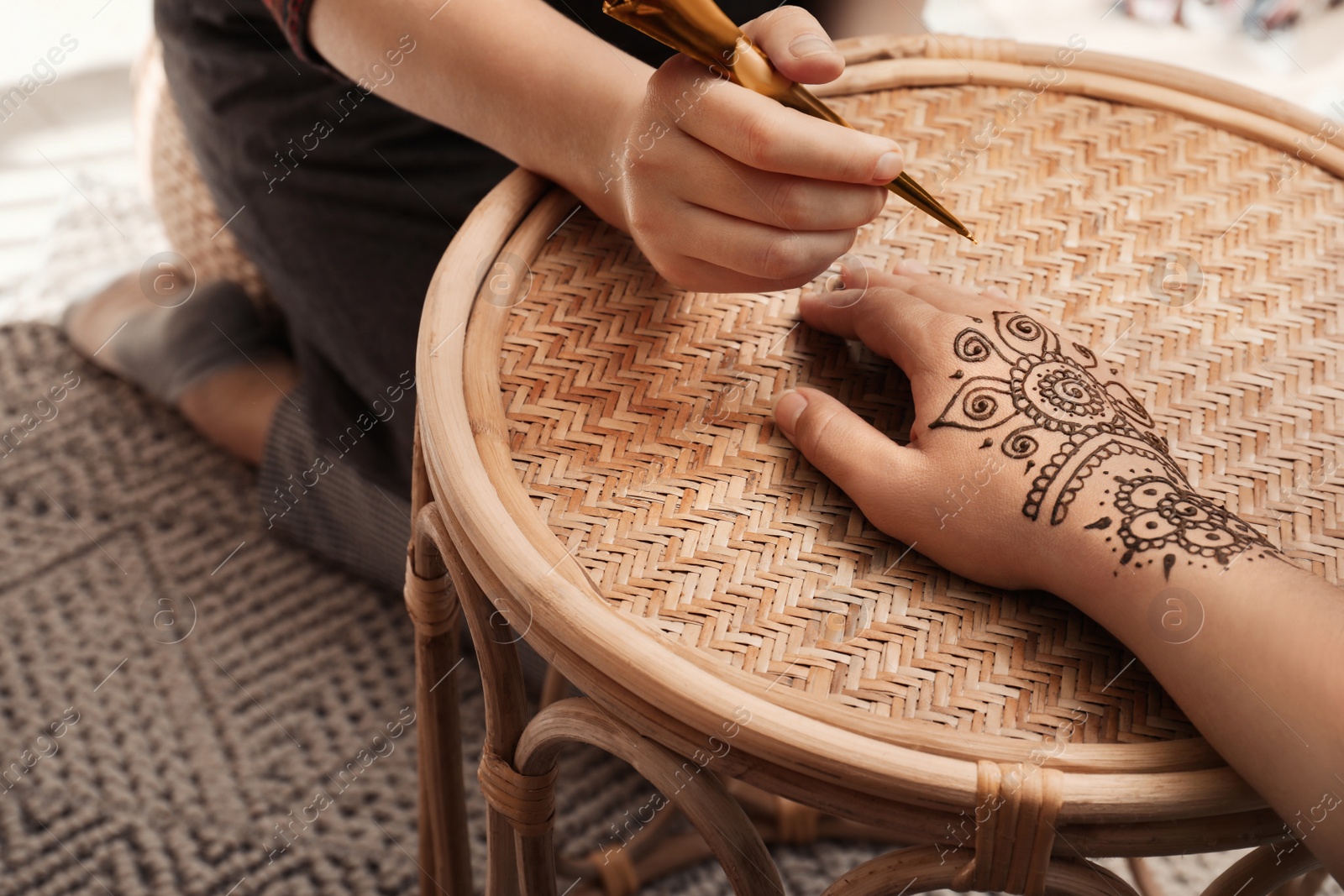 Photo of Master making henna tattoo on hand at table, closeup. Traditional mehndi