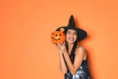 Photo of Beautiful woman wearing witch costume with Jack O'Lantern candy container for Halloween party on yellow background, space for text