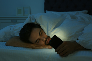 Photo of Young man addicted to smartphone in bed at night