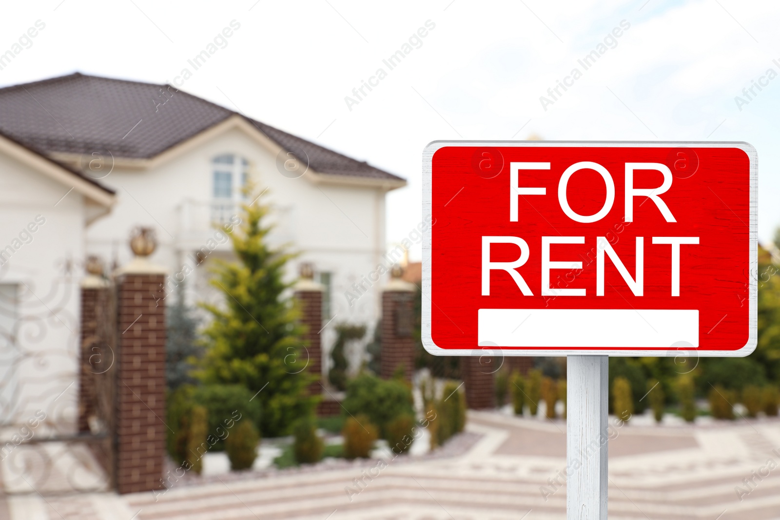 Image of Sign with phrase FOR RENT and blurred view of beautiful house