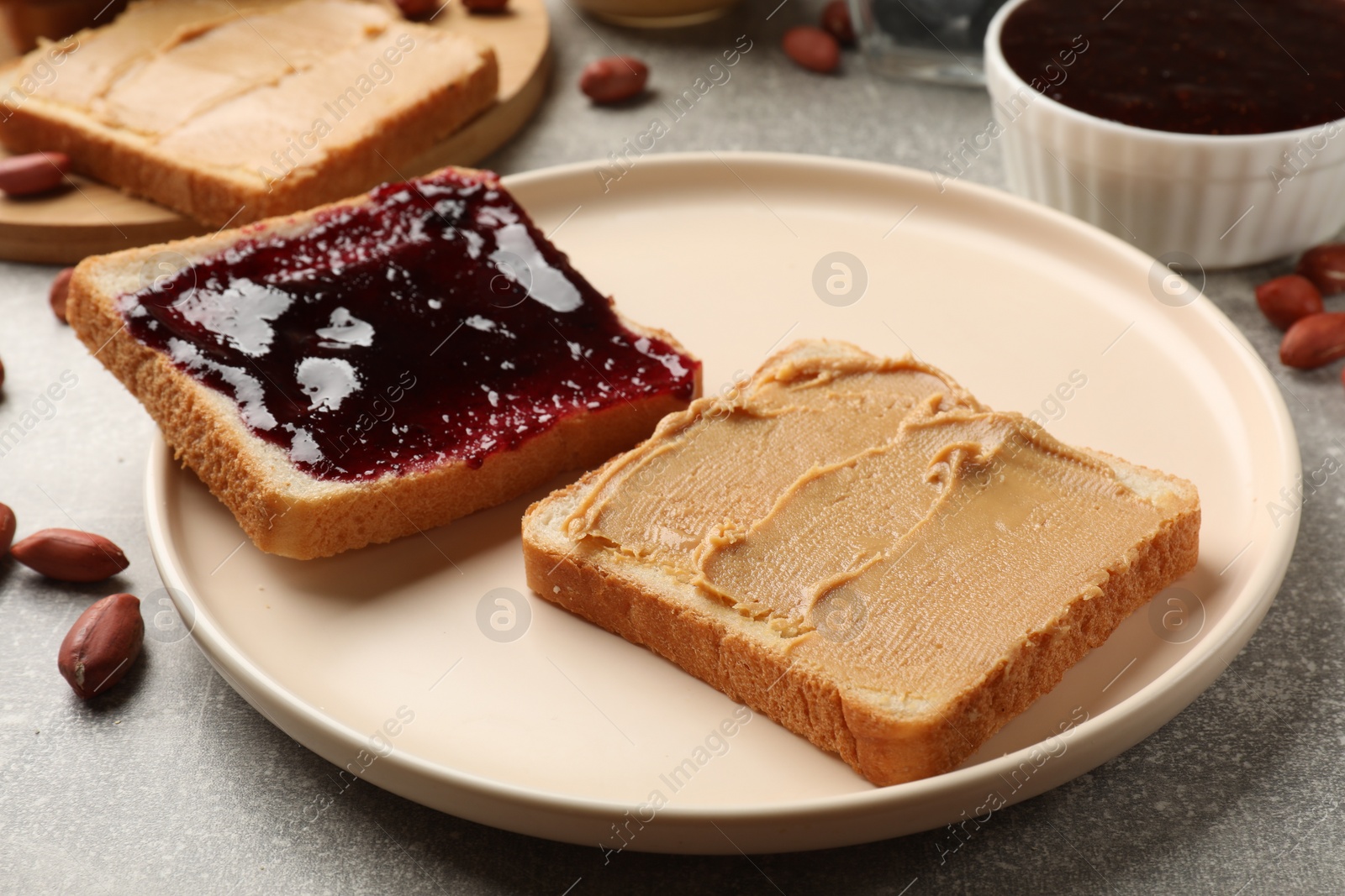 Photo of Tasty peanut butter sandwiches with jam on gray table, closeup