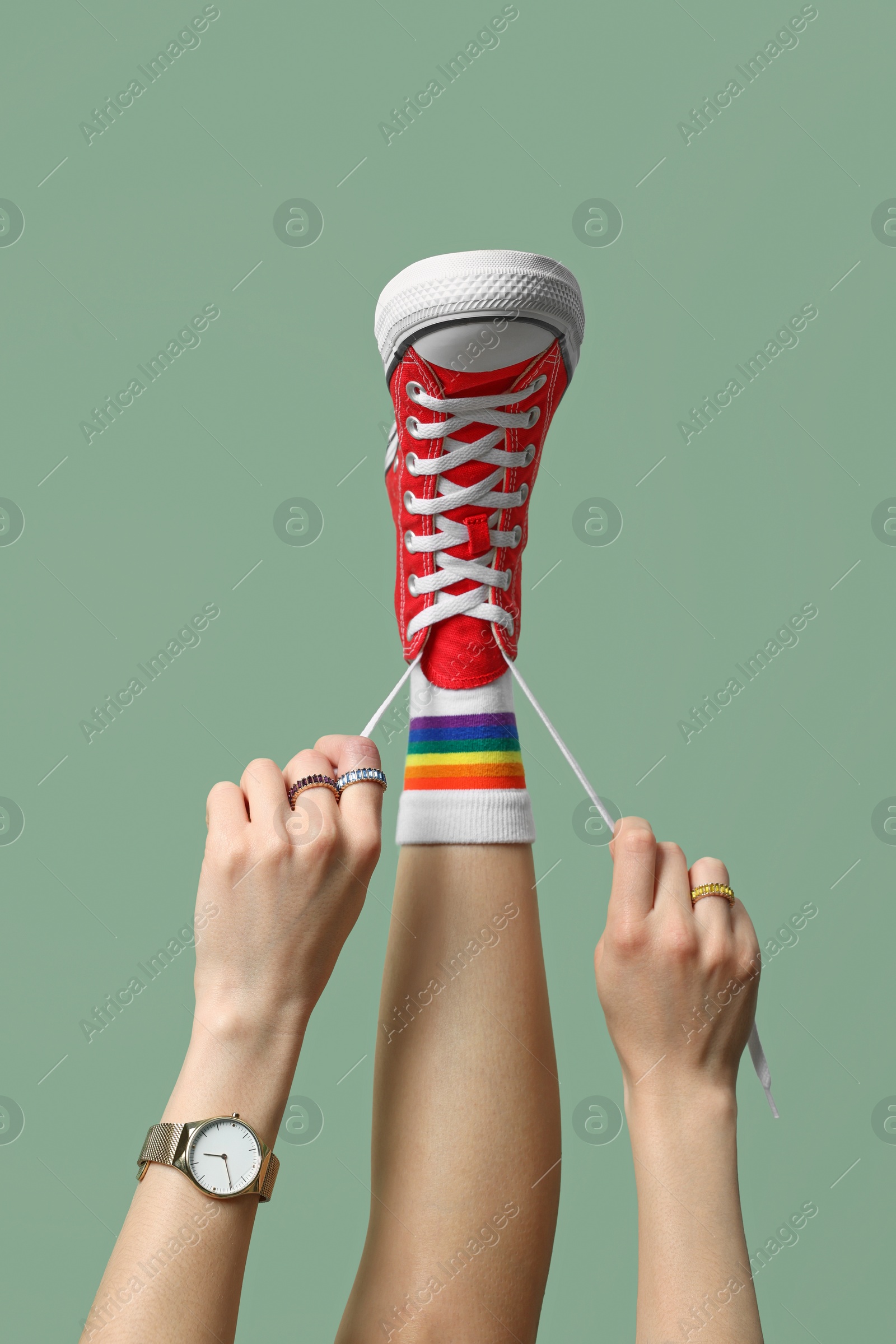 Photo of Woman tying laces of stylish gumshoe on pale green background, closeup