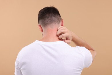 Photo of Allergy symptom. Man scratching his neck on light brown background, back view