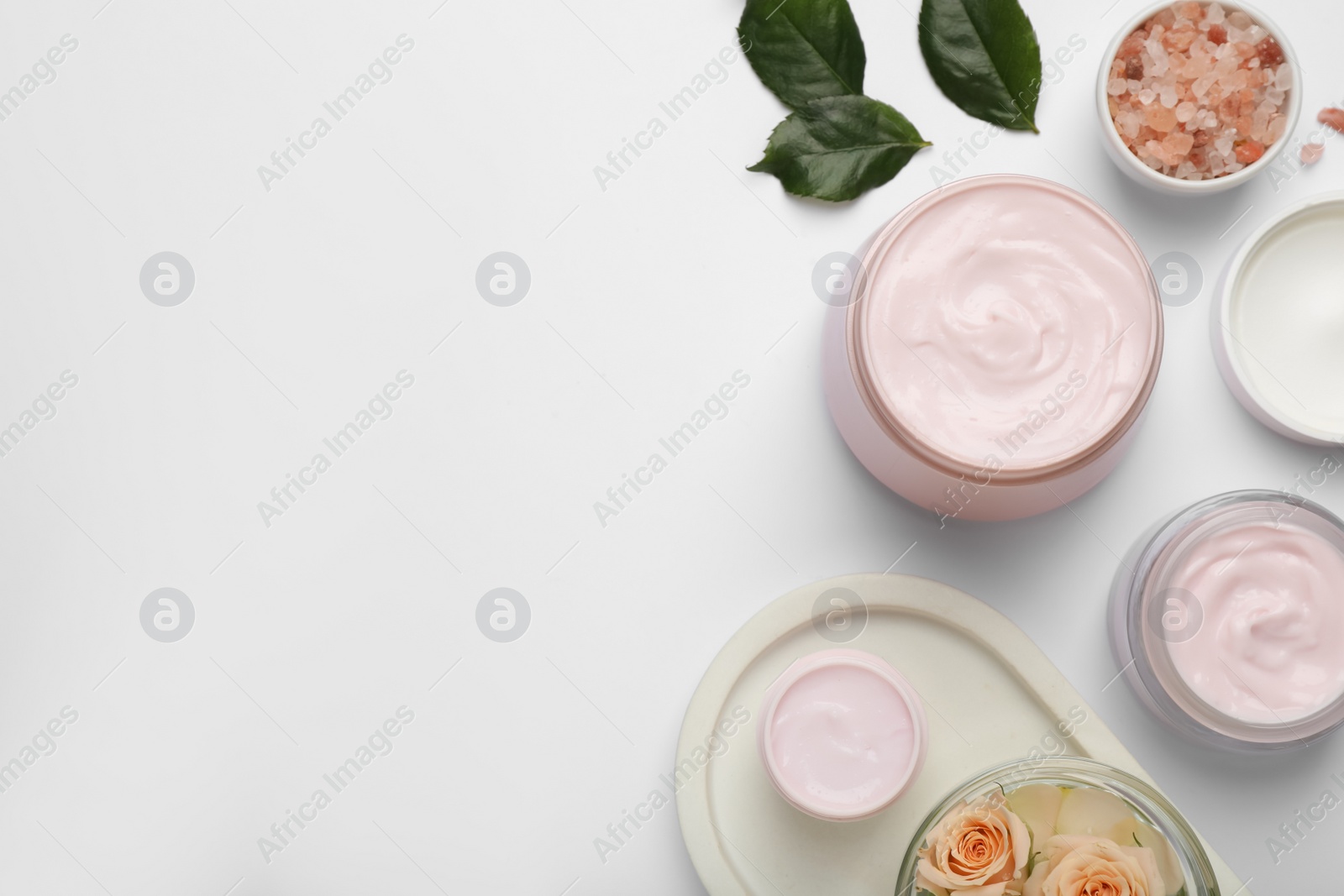 Photo of Body cream and other cosmetic products with rose on white background, top view. Space for text