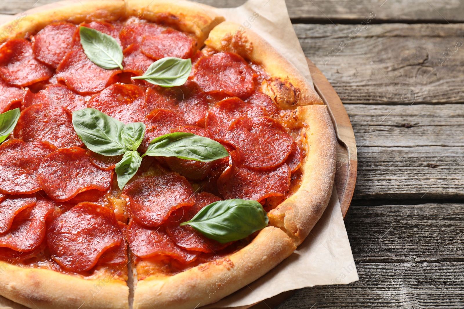 Photo of Tasty pepperoni pizza with basil on wooden table, closeup. Space for text