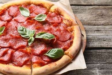 Tasty pepperoni pizza with basil on wooden table, closeup. Space for text