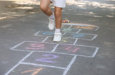 Photo of Little child playing hopscotch drawn with chalk on asphalt outdoors, closeup