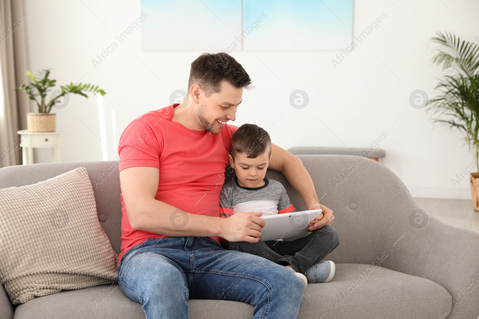 Photo of Boy and his father with tablet sitting on sofa at home. Family time