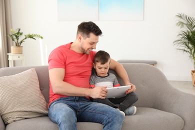 Boy and his father with tablet sitting on sofa at home. Family time