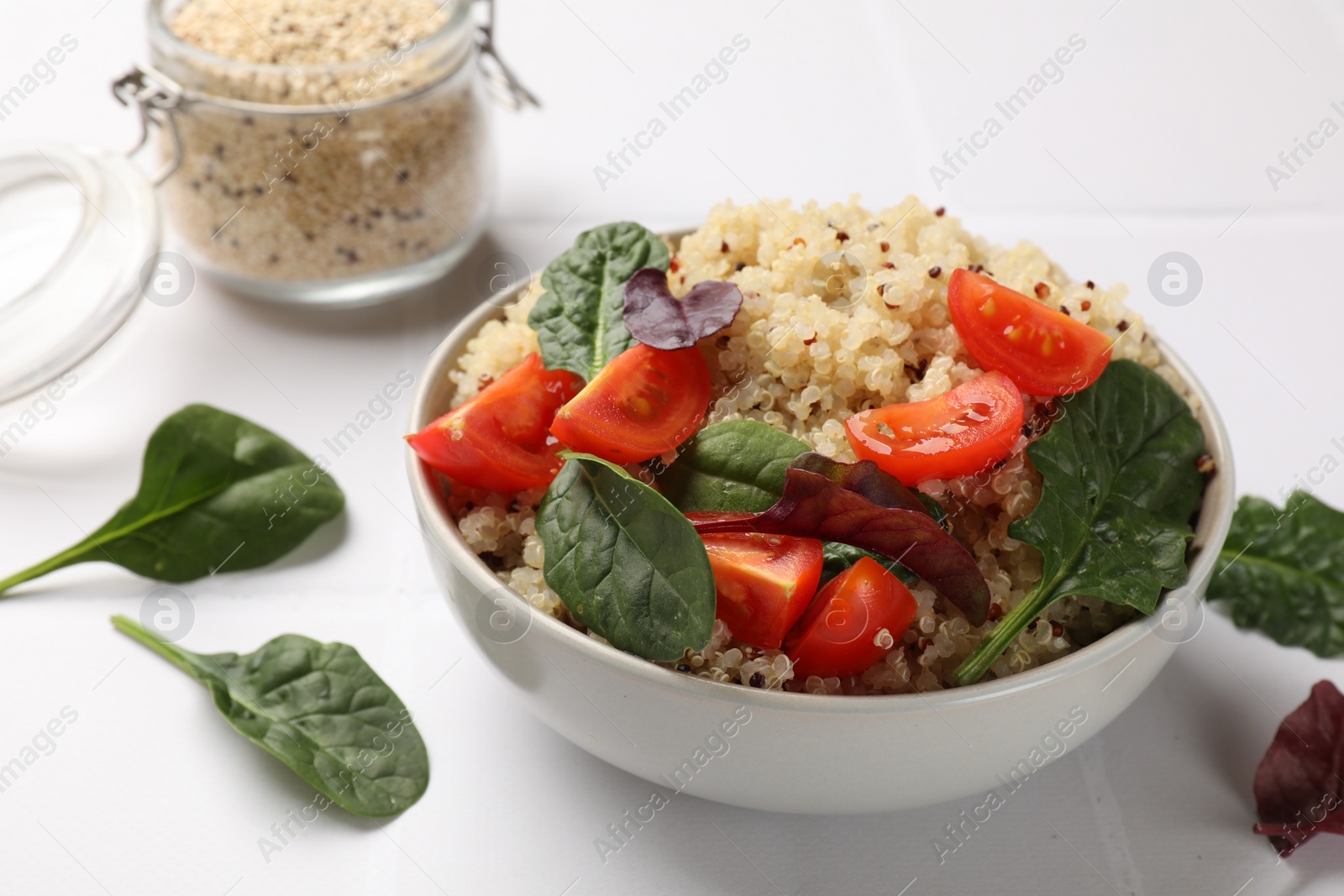 Photo of Tasty quinoa porridge with tomatoes and spinach in bowl on white table, closeup