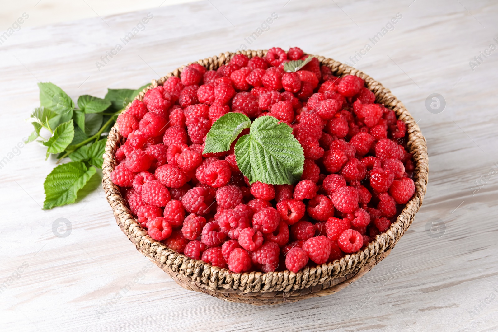Photo of Tasty ripe raspberries and green leaves on white wooden table