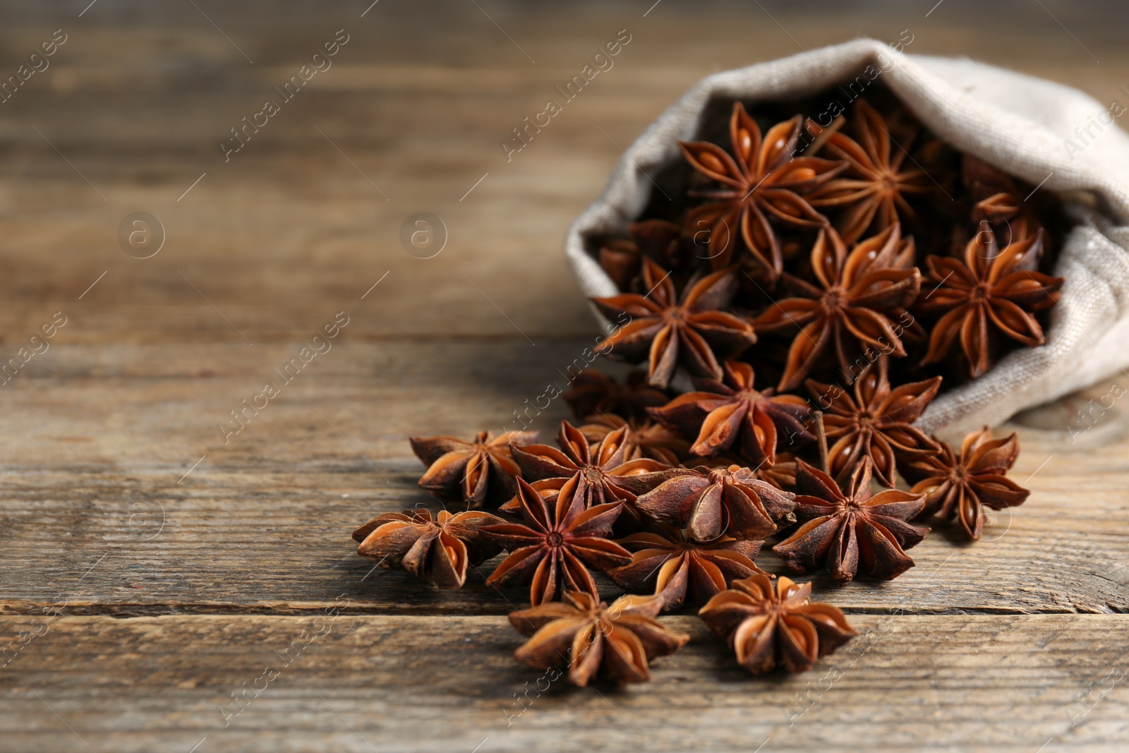 Photo of Overturned bag with aromatic anise stars on wooden table, closeup. Space for text