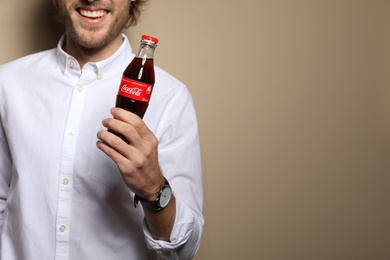 MYKOLAIV, UKRAINE - NOVEMBER 28, 2018: Young man with bottle of Coca-Cola on color background, closeup. Space for text