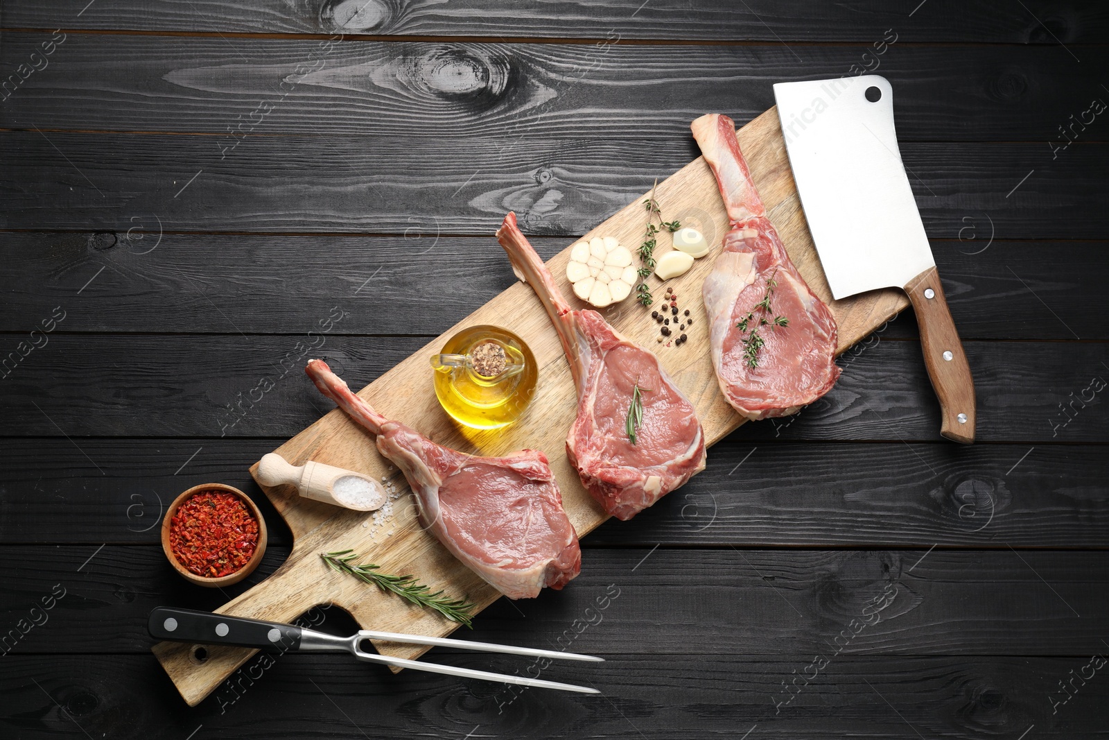 Photo of Fresh tomahawk beef cuts, spices and butcher tools on black wooden table, top view