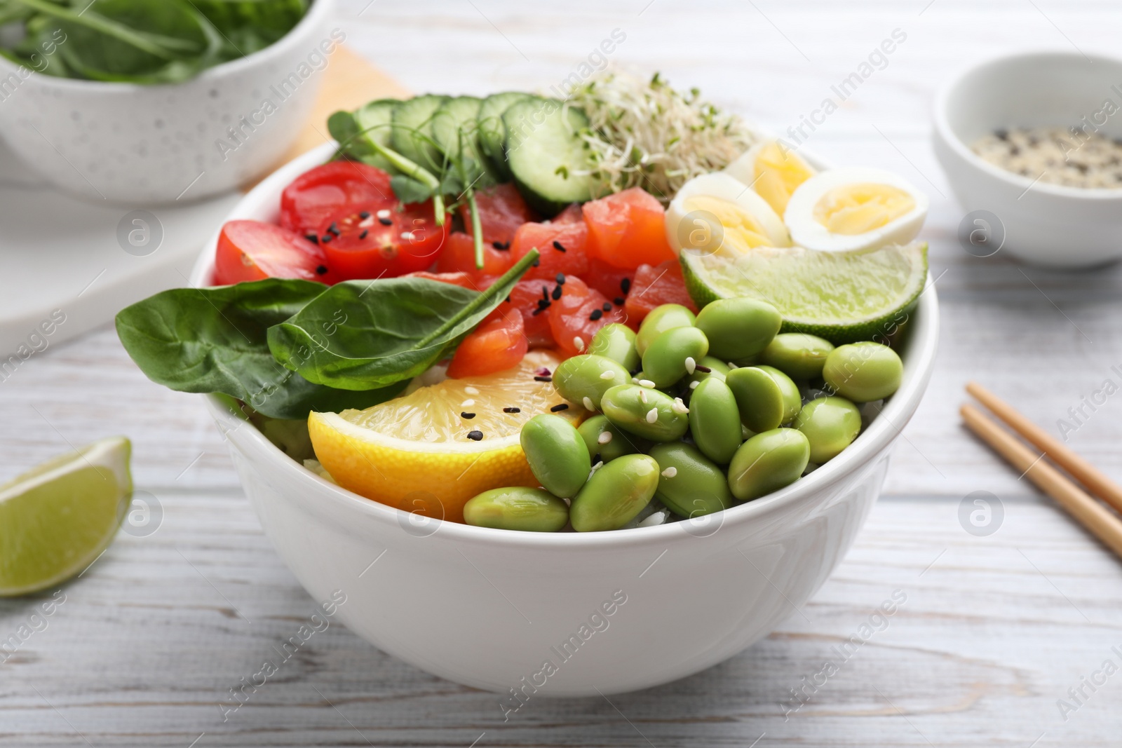 Photo of Delicious poke bowl with quail eggs, fish and edamame beans on white wooden table