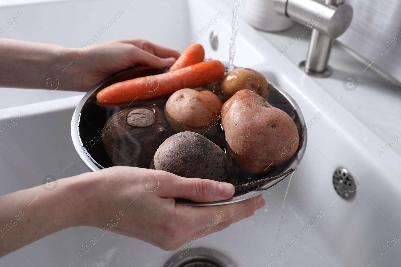 Photo of Woman washing fresh vegetables in kitchen sink, closeup. Cooking vinaigrette salad