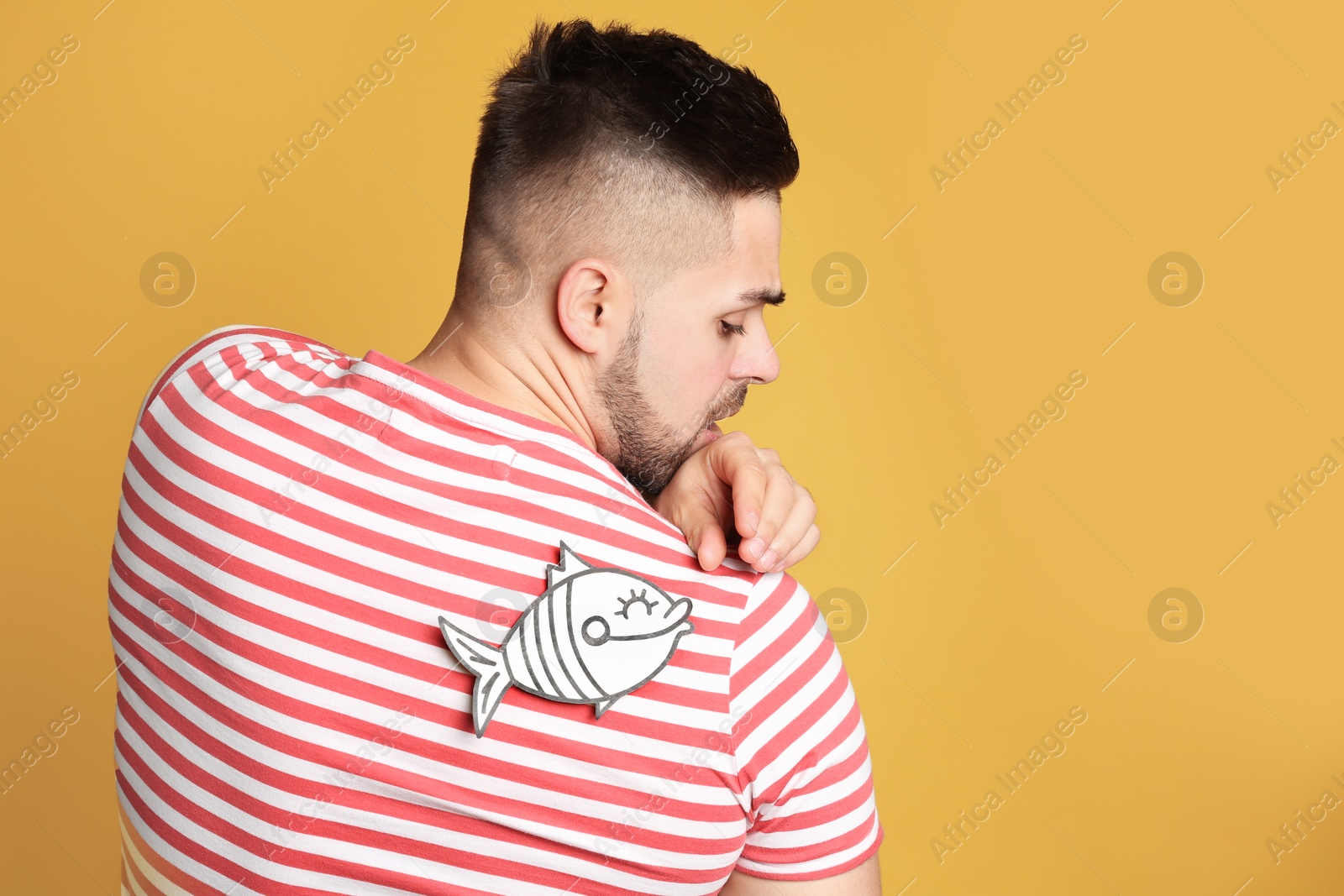 Photo of Man with paper fish on back against yellow background. April fool's day