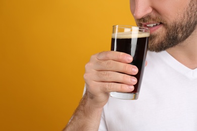 Young man with cold kvass on yellow background, closeup. Traditional Russian summer drink