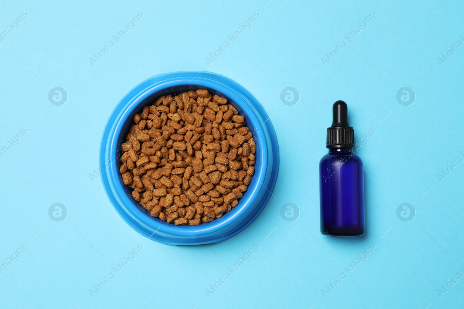 Photo of Glass bottle of tincture near bowl with dry pet food on light blue background, flat lay