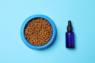 Photo of Glass bottle of tincture near bowl with dry pet food on light blue background, flat lay