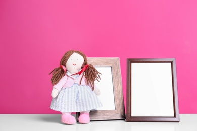 Photo of Photo frames and adorable doll on table against color background, space for text. Child room elements