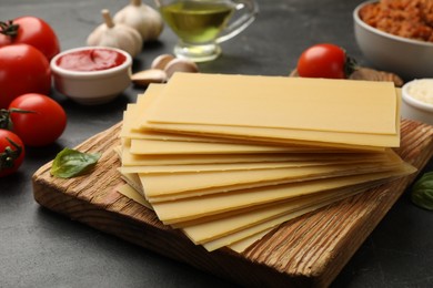 Photo of Cooking lasagna. Wooden board with pasta sheets and products on dark table, closeup
