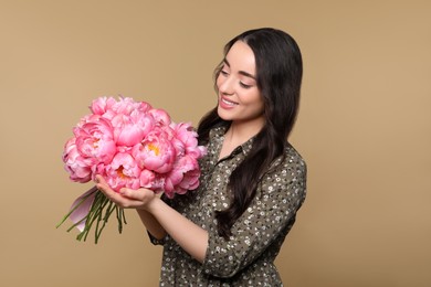 Photo of Beautiful young woman with bouquet of pink peonies on light brown background