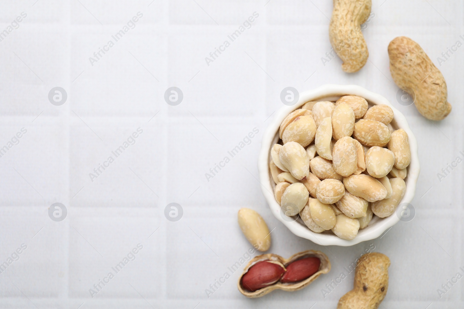 Photo of Fresh peeled peanuts in bowl on white tiled table, flat lay. Space for text