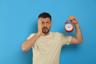 Emotional man with alarm clock on light blue background. Being late concept