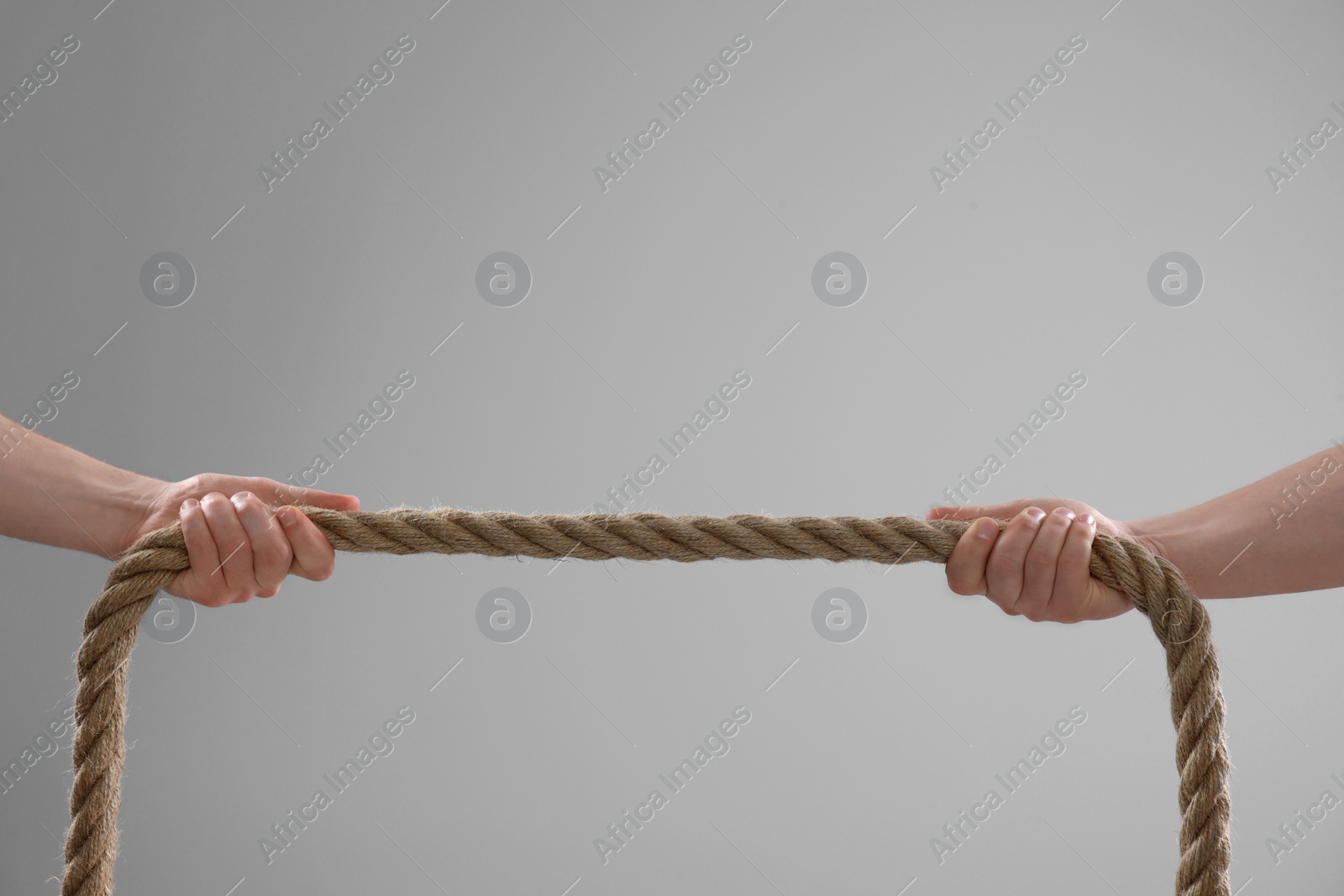 Photo of Dispute concept. Men pulling rope on light grey background, closeup