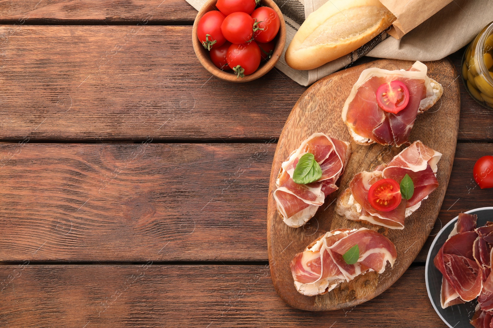 Photo of Board of tasty sandwiches with cured ham, basil and tomatoes on wooden table, flat lay. Space for text