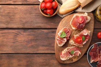 Board of tasty sandwiches with cured ham, basil and tomatoes on wooden table, flat lay. Space for text