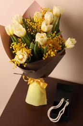 Bouquet with beautiful spring flowers and necklace on wooden table