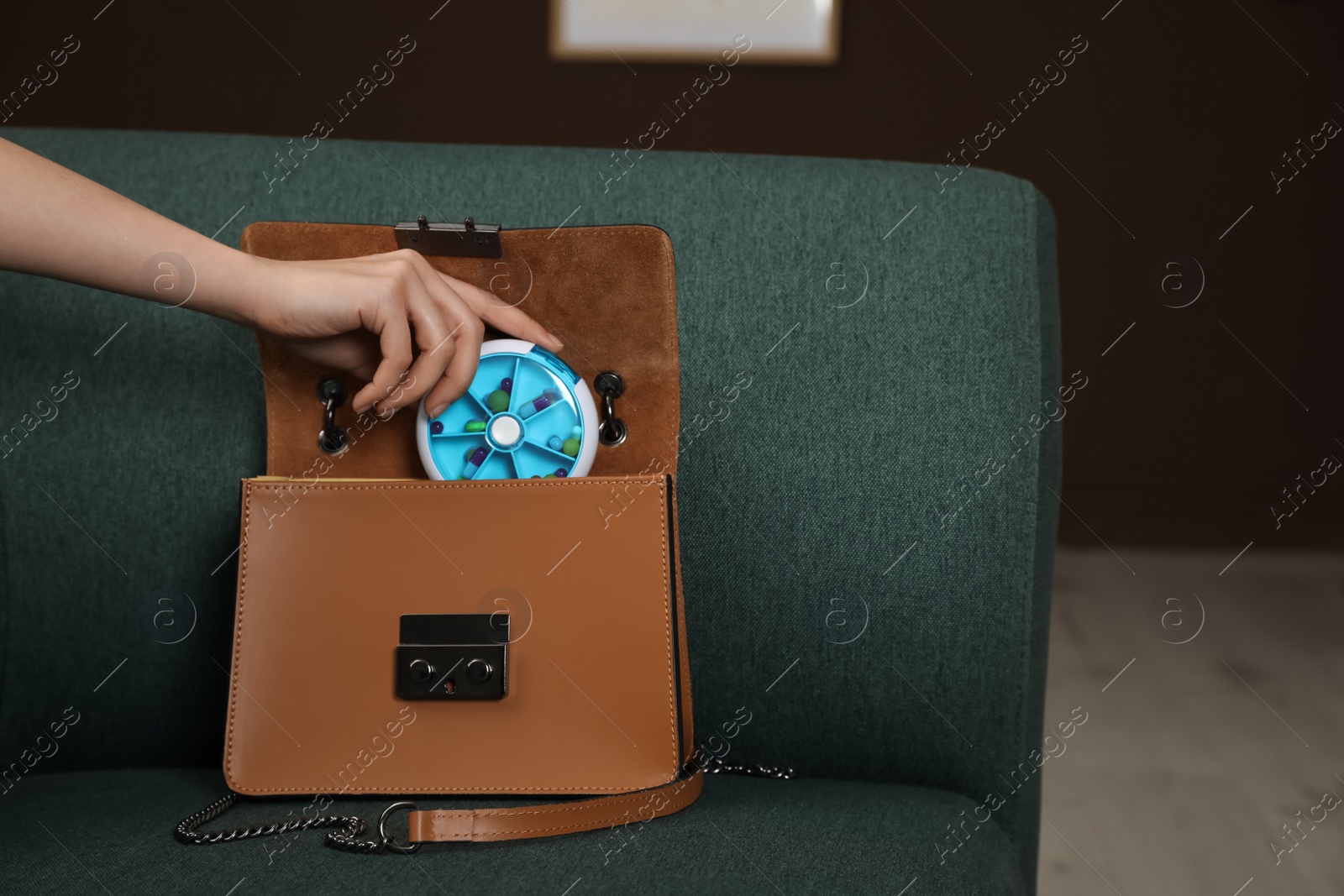 Photo of Woman putting plastic box with pills into bag on sofa indoors, closeup. Space for text