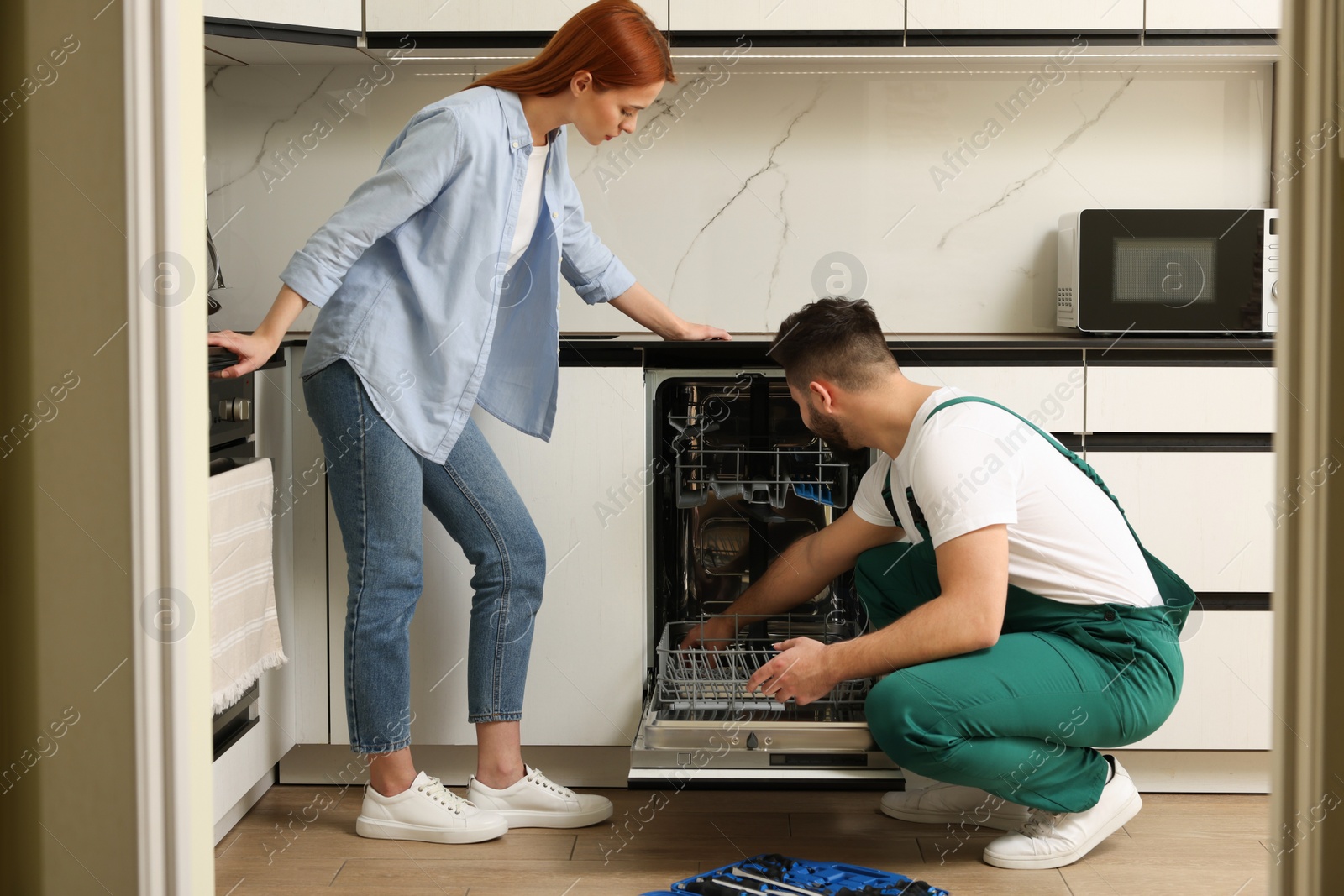 Photo of Woman looking how serviceman repairing her dishwasher in kitchen