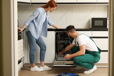 Woman looking how serviceman repairing her dishwasher in kitchen