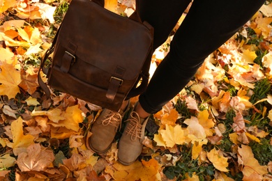 Photo of Woman holding bag in park with fallen leaves, closeup. Autumn season
