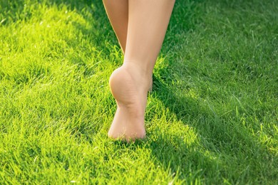 Teenage girl walking barefoot on green grass outdoors, closeup