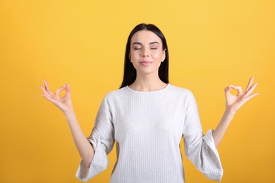 Photo of Young woman meditating on yellow background. Stress relief exercise