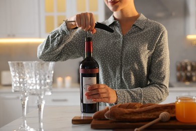 Photo of Romantic dinner. Woman opening wine bottle with corkscrew at table in kitchen, closeup