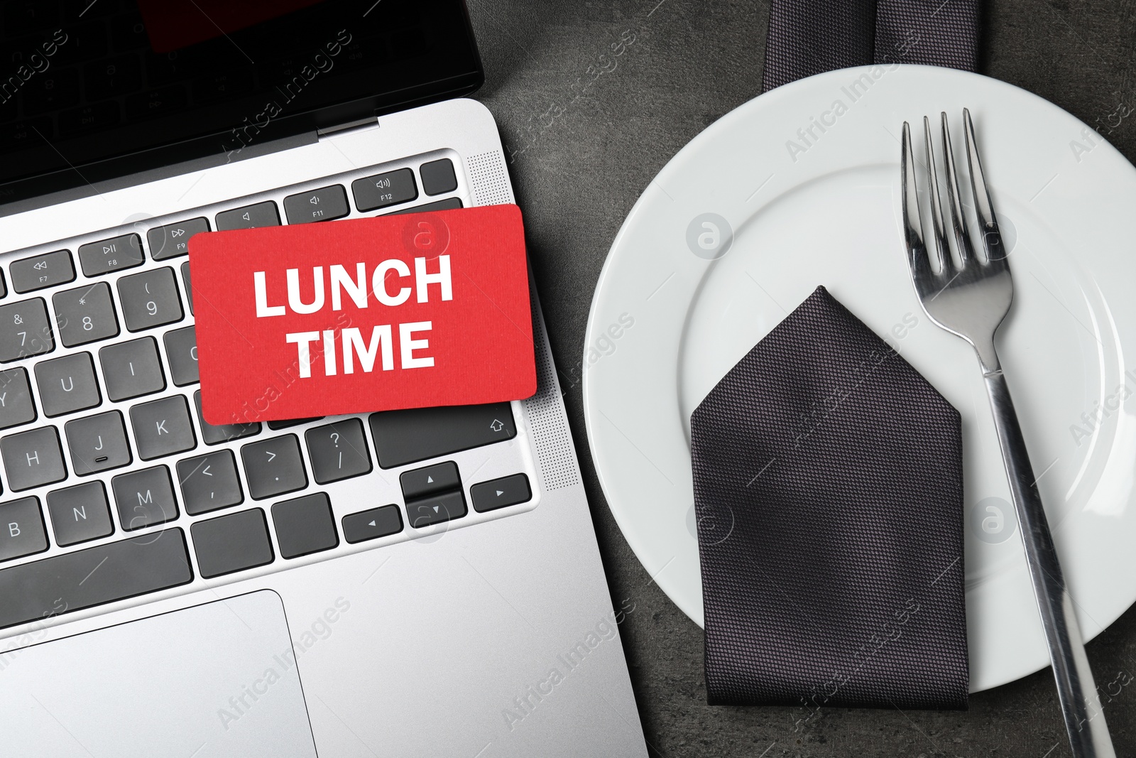 Image of Business lunch time. Laptop, card, plate, fork and tie on gray table, flat lay