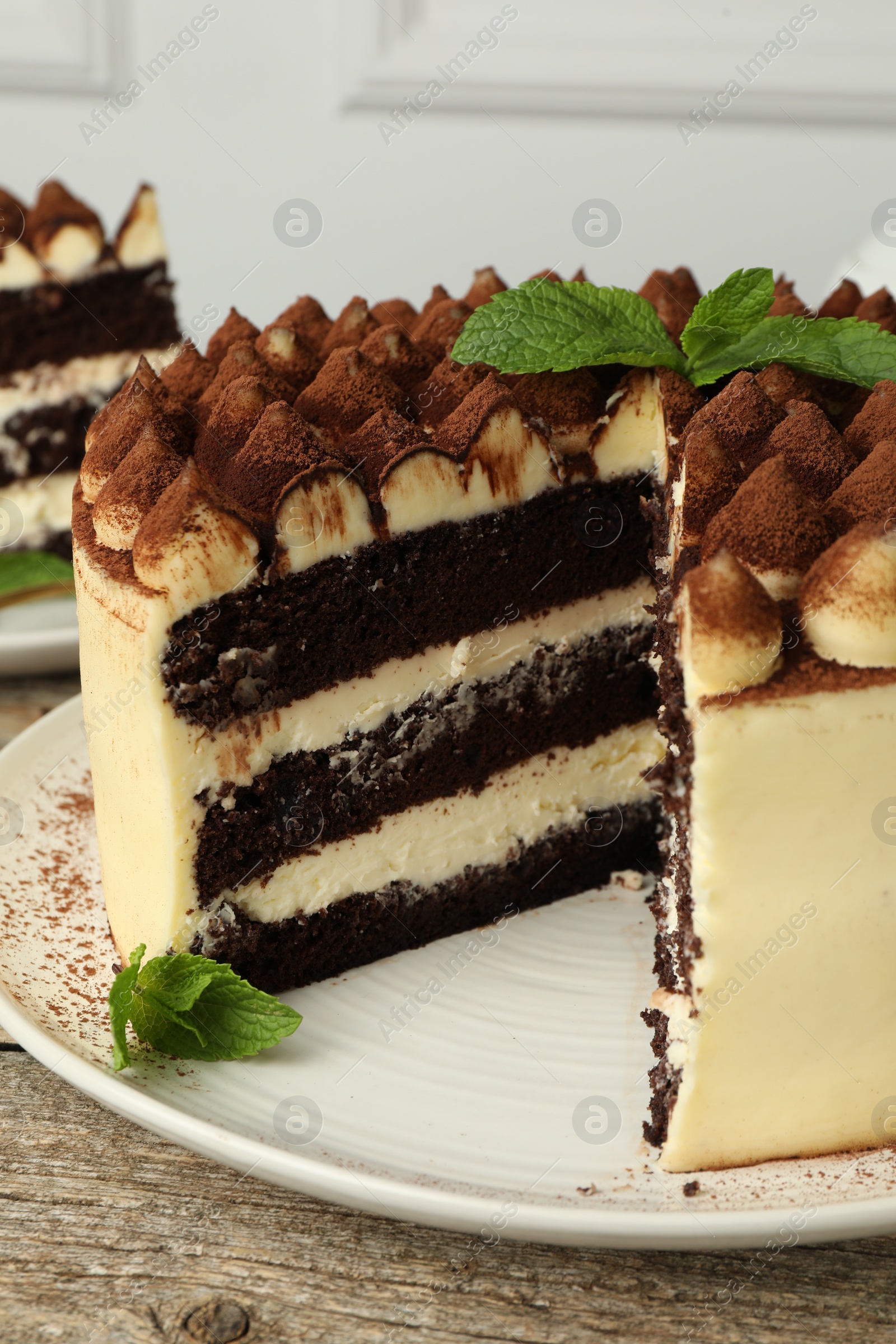 Photo of Delicious tiramisu cake with cocoa powder and mint leaves on wooden table, closeup