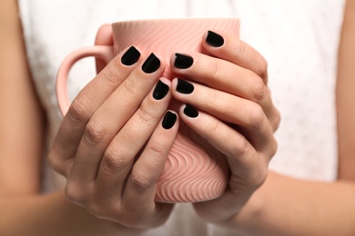 Photo of Woman with black manicure holding cup, closeup. Nail polish trends