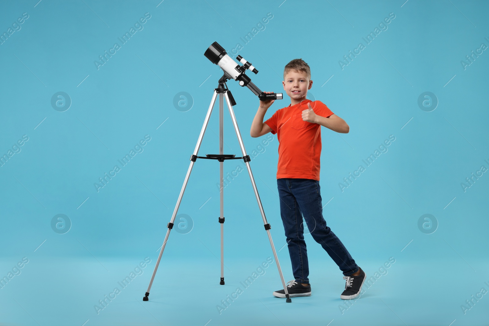 Photo of Happy little boy with telescope showing thumb up on light blue background