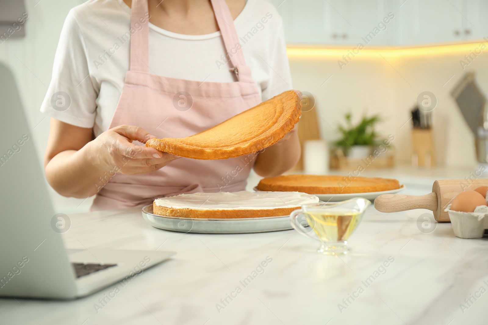 Photo of Woman making cake while watching online cooking course via laptop in kitchen, closeup