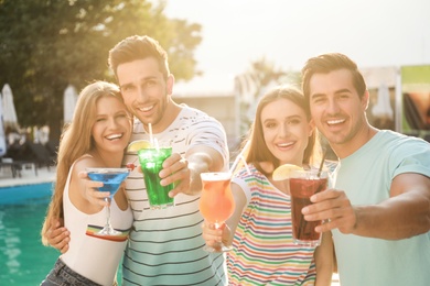 Happy young friends with fresh summer cocktails relaxing near swimming pool