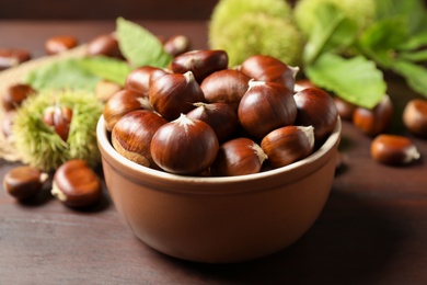 Photo of Fresh sweet edible chestnuts on brown wooden table, closeup